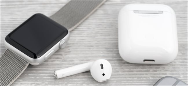 AirPods and their charging case next to an Apple Watch.