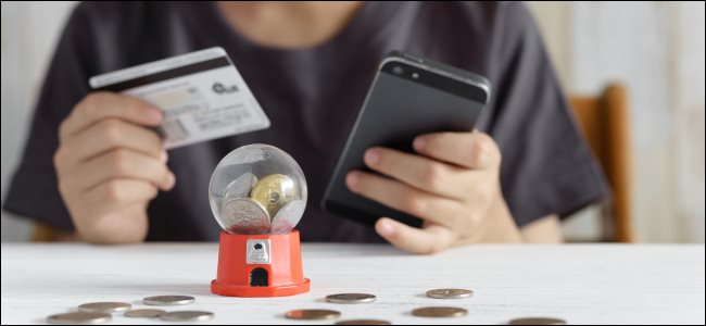 A kid's hands holding a credit card and a smartphone, and a gacha game on the table.