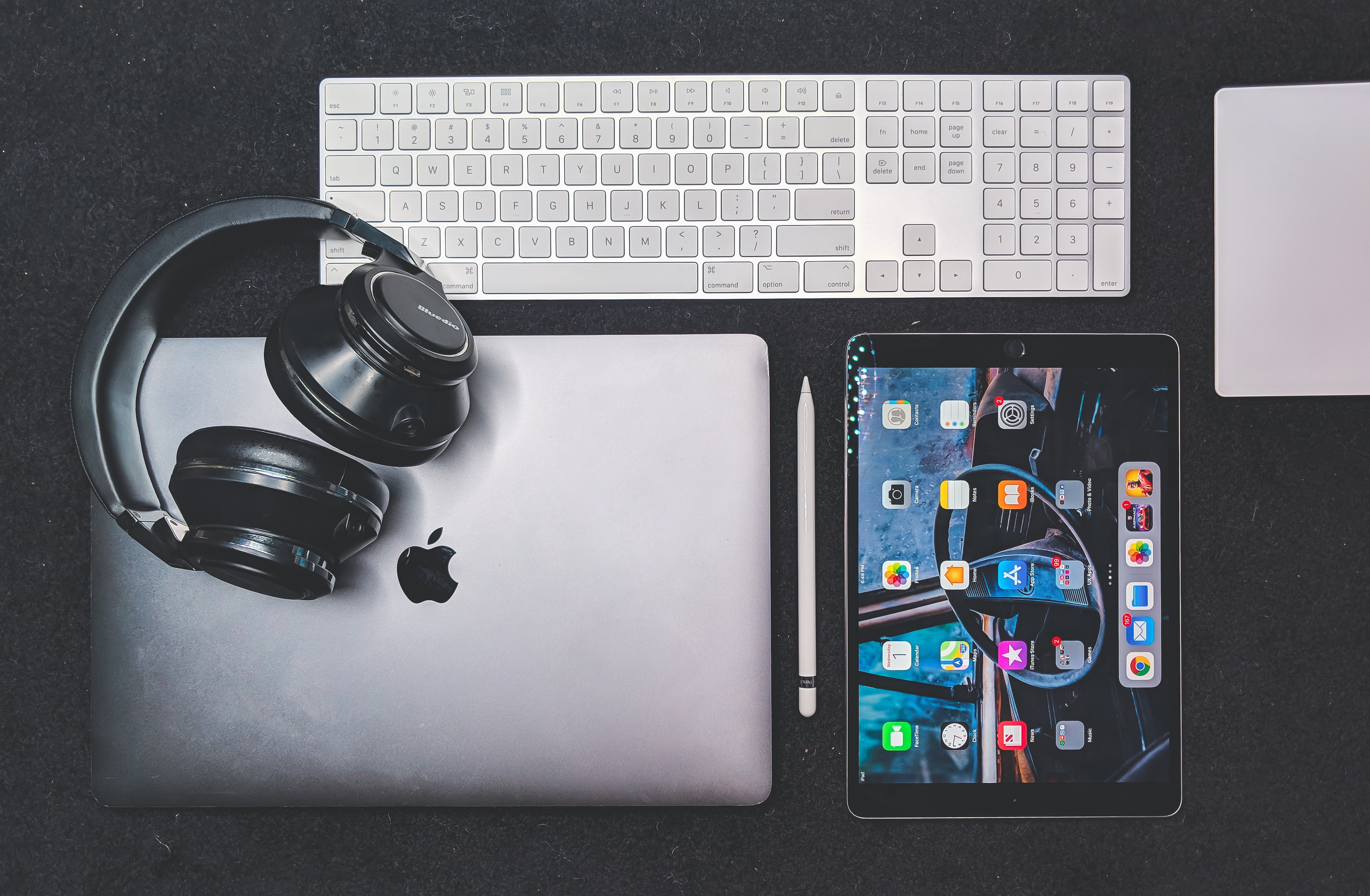 a picture of desktop with macbookpro, headphone, iPad Pro and Keyboard.