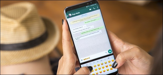 A woman's hands holding a smartphone and typing emojis in WhatsApp.