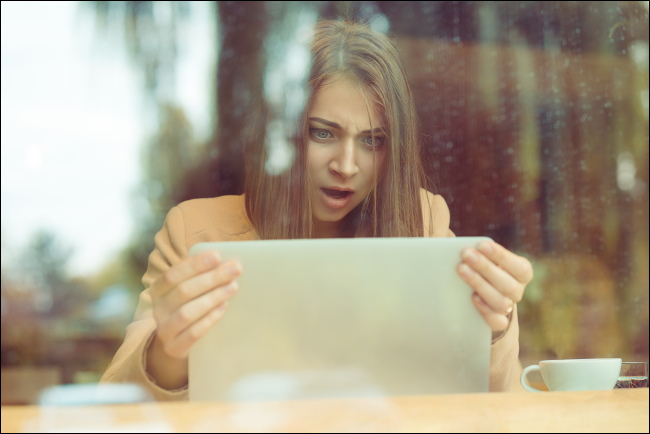 A shocked woman holding her laptop's screen.