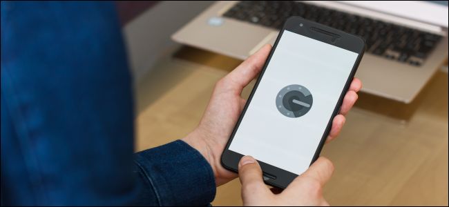 A man's hands holding a phone with the Google Authenticator app on the screen.