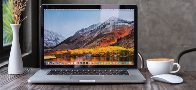 A MacBook Pro open on a table next to a mug and a vase of flowers. 