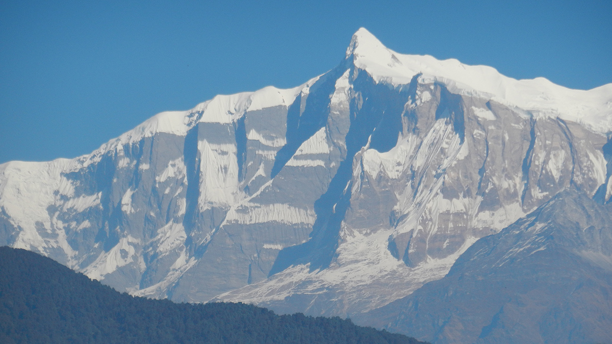 一座中间有尖峰的雪山脊坐落在明亮的蓝天前面。